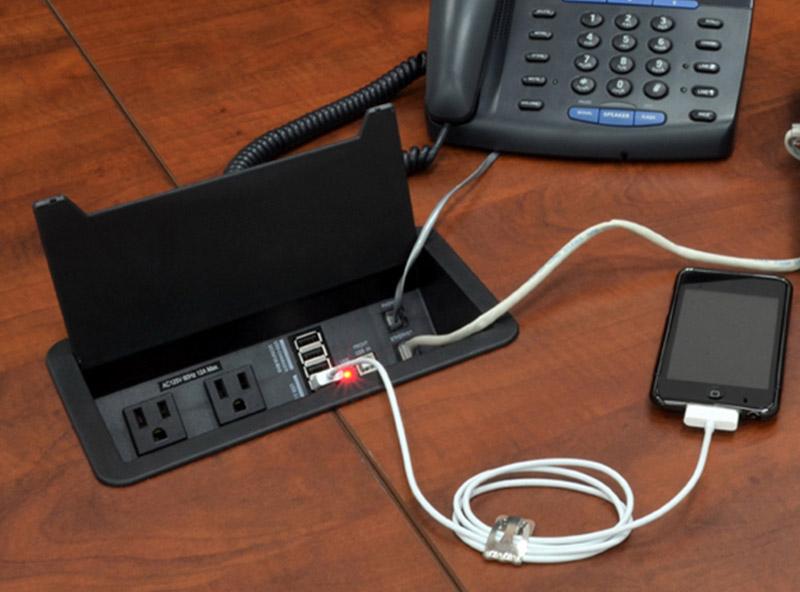- A black phone and an Iphone connected to the power data grommet on a conference table