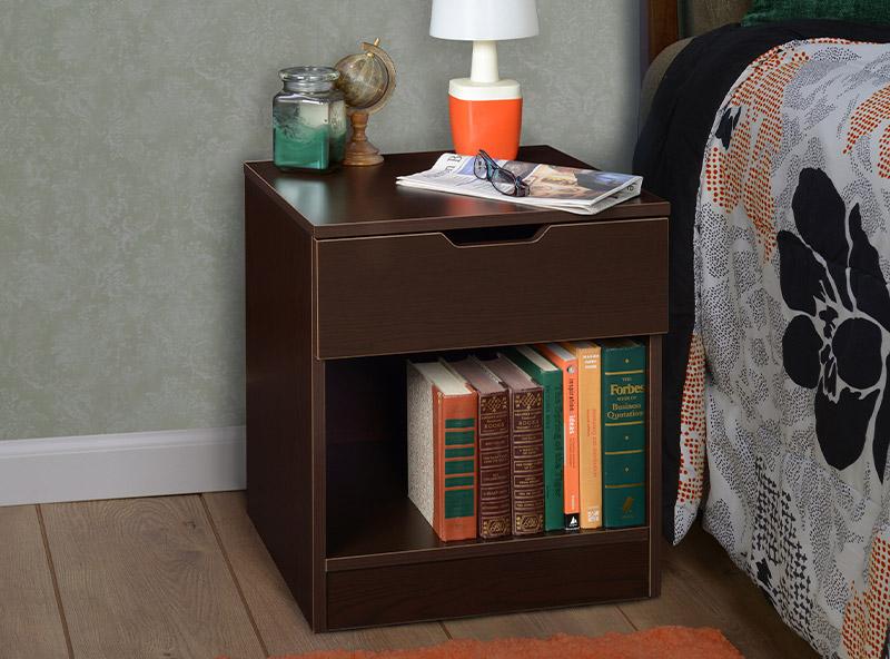 - bedroom night stand with one drawer with a lamp on top of the stand next to a bed