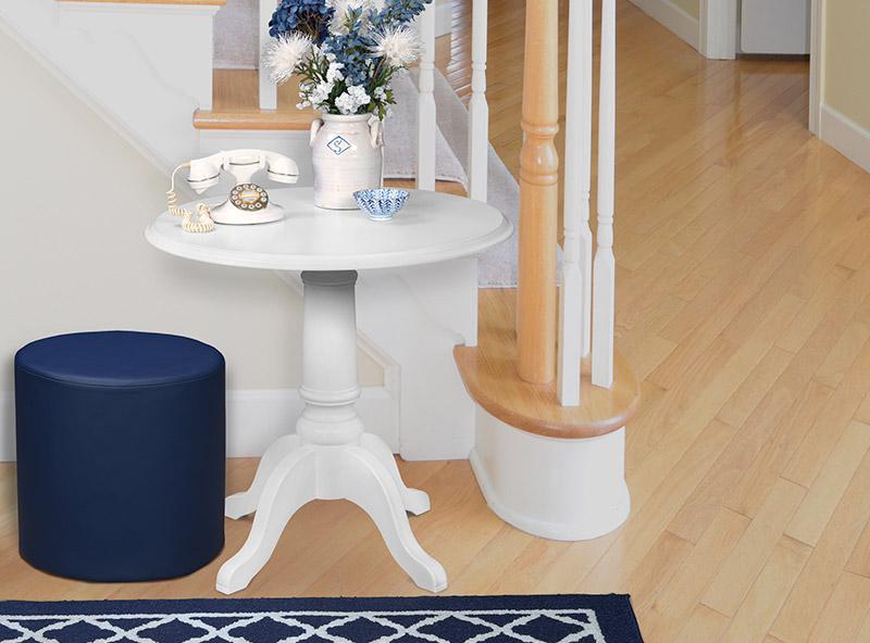 42 inch round pedestal table holding a flower pot and phone next to a navy ottoman
